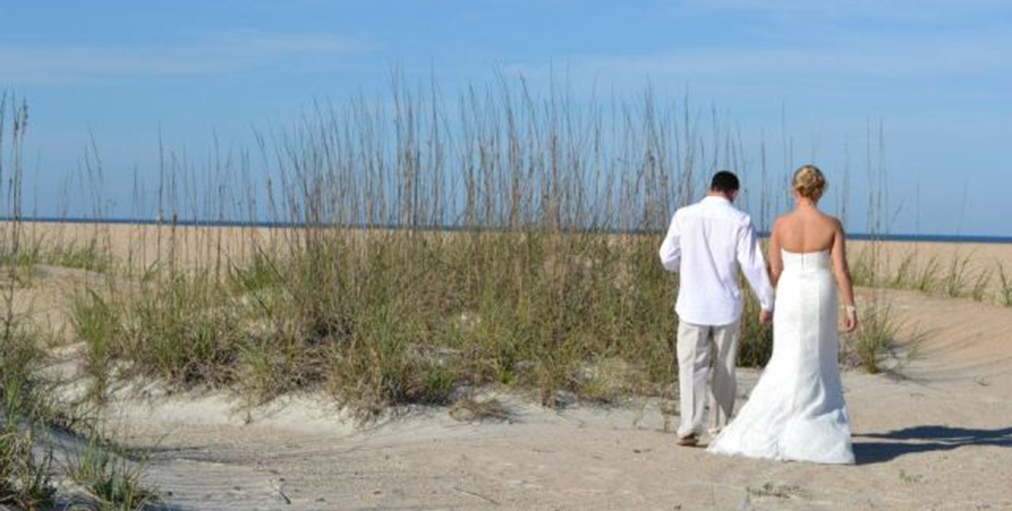 couple in wedding outfits walking on beach 